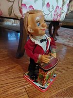 Side angle showing the bartender character with red fabric jacket, plastic head, holding a glass, and decorated tin base labeled 'Bartender'.