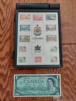 Photo of a collector's case containing 12 Canadian Centennial postage stamps arranged around the Canadian coat of arms, plus a Canadian one dollar bill from 1967.