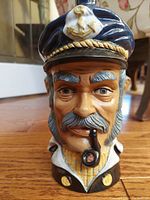 Front close-up view of the ceramic bust decanter showing detailed facial features, navy captain's hat with gold anchor detail, and pipe in mouth.