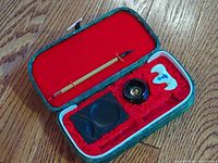 Open box showing calligraphy brush, ink stone, ink container and ceramic brush rest inside red velvet compartment.