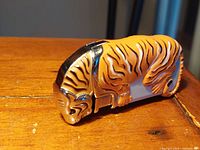 Side view of tiger-shaped lighter showing painted stripes, metallic accents, and compact size on wood surface.