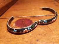 Photo showing the bracelet laid flat with detailed floral cloisonné enamel and visible clasp, on a wooden surface.