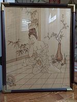 Frontal photo showing the detailed wood engraving of an oriental woman in a traditional room with bamboo blind and objects, framed with wood and brass accents.