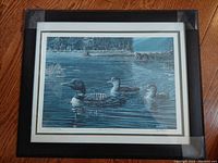 Full view of framed vintage limited edition print showing loons on a lake with forest background, under glass in wood frame.