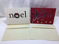 Front view of two Christmas cards 'noel' and 'joy' with their envelopes shown below