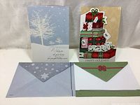 Two large Christmas cards with decorative envelopes displayed side-by-side on a white surface.