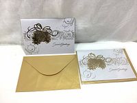 Two large white Christmas cards with embossed gold pinecone designs and gold envelopes shown on white background