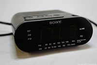 Front angle view showing green LED time display, Sony logo, and frequency markings for FM/AM bands on the front panel of the clock radio.