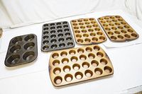 Five vintage muffin trays displayed together on white surface; four trays with 24 cavities each and one tray with 6 large cavities