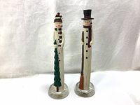Full view of two tall vintage snowman pencil holder figurines on clear circular bases against white background