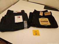 Two folded pairs of pants on table with tags visible, one Tommy Hilfiger Twill Pant and one Kirkland Signature Jeans.