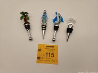Four art glass wine bottle stoppers displayed in a row on a white background with auction label.