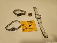 Four pre-owned watches displayed on a flat surface with a MaxSold tag showing lot number 19.