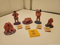 Photo of all five clay pig sculptures arranged in a line with original tags visible in front of four of them.