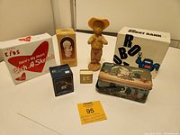 Grouped view of all collectible items showing boxed Avon Robot Bank, Etch A Sketch, E.T. Pot Pal, E.T. pin, Boy Figurine, Precious Moments figurine, and Girls Scouts tin lunch pail.
