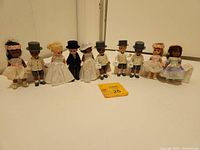 Wide view of 10 Madame Alexander dolls arranged in a row showcasing wedding themed attire, including brides, grooms, and other wedding party members.