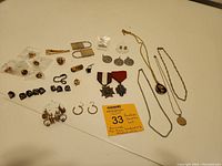 Overview of all jewelry items arranged on surface showing earrings, tie pins, medals, necklaces, and medallion with chain.