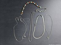 Full view of all five silver jewelry pieces including necklaces and bracelets on black background.