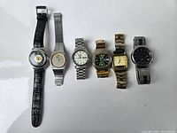 Six vintage wristwatches laid out in a row on a white background, showing varied styles and bracelets.