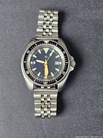 Front view of the men's dive watch showing black dial, luminous markers and hands, orange minute hand, and stainless steel bracelet.