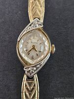 Close-up of the gold plated Bulova ladies watch face showing textured crystal, gold tone markers, and decorative casing edges.