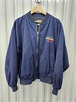 Front view of navy blue vintage Firestone Racing jacket with zipper and ribbed collar, cuffs, and waistband on wooden hanger.