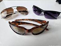 Three pairs of Oakley sunglasses with tortoiseshell, metal aviator, and black frames, showing lens marks.