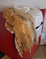 Three knitted scarves draped over a red surface showing different colors and textures