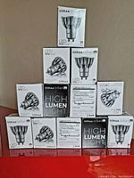 Photo showing 12 boxes of SORAA GU10 LED lights stacked in a pyramid formation against a neutral background, all new in box and sealed.
