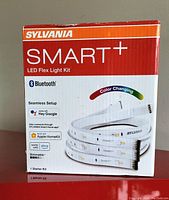 Front photo of SYLVANIA SMART+ LED Flex Light Kit packaging showing Bluetooth, compatible voice assistants, and color changing feature.