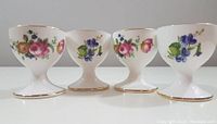 Front view of four Oakley floral egg cups with gold rims lined up.
