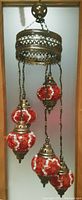 Full view of the hanging ceiling fixture showing the antique brass top mount, the circular framework, chains and five mosaic glass bulbs hanging from it. The bulbs are red with white mosaic patterns and brass fittings.