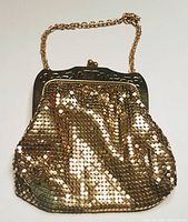 Full front view of vintage golden metallic mesh evening bag hanging from its chain handle on a white background.
