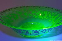 Uranium glass bowl glowing bright green under UV light showing optic fluorescence and detailed applied scroll and leaf pattern