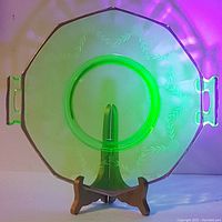 Uranium glass serving dish glowing green under UV light revealing its uranium content. Octagonal shape with two handles and etched wreath patterns.