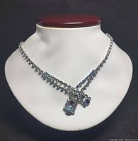 Front view of the vintage signed Continenal rhinestone necklace displayed on a white bust. Shows the double strand chain with blue and clear stones, and the decorative front cluster.