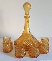 Full set of vintage amber glass Empoli decanter with stopper and six matching shot glasses arranged in front.