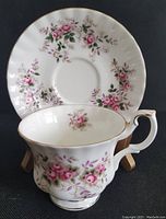 Front view of Royal Albert Lavender Rose bone china tea cup with the matching saucer placed vertically behind it, showing the floral pattern and gold trim details clearly.