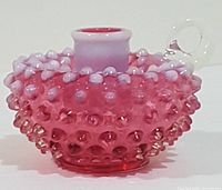Front-side view showing cranberry hobnail pattern, opalescent white rim and candle socket, and clear handle loop.