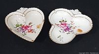 Two hand painted porcelain trinket dishes, heart and clover shaped, showing floral designs and gold trim.