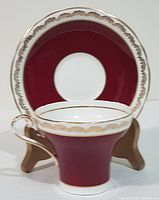 Front view of Aynsley corset shaped teacup with matching saucer, showing burgundy body and gold trim.