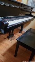 Left-side view of baby grand piano showing keyboard, pedals and bench