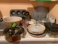 Photo showing metal muffin tin, large ceramic mixing bowl, springform pans, glass mixing bowls, metal kitchen utensils, cutting board, and pizza pan on countertop.