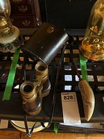 Photo showing the vintage brass and leather binoculars with leather carrying case and one letter opener with curved handle on a black metal table.