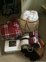 Photo showing all items in the lot: sheet set in box, feather down duvet in carrying bag, plaid Sherpa throw and cushion, Afghan, two rolled throws