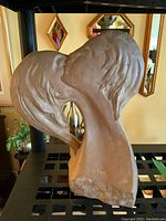 Front view of clay bust sculpture showing kissing couple with detailed hair and facial features.