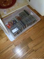 Plastic tote filled with a variety of music CDs in jewel cases neatly arranged.