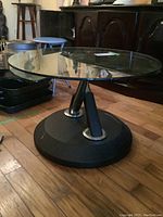 Side angled view showing round glass top and heavy black metal base with angled supports.