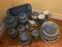 Full view of the complete set showing meat platter, canisters, teapot, cream and sugar set, salt and pepper shakers, cups, mugs, bowls, luncheon plates, and dinner plates stacked.