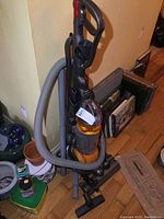 Full view of Dyson DC25 vacuum with hose and accessories standing upright with some household items around it.